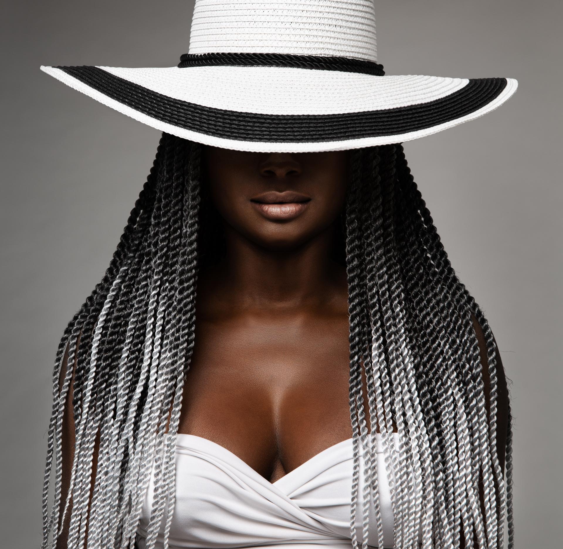 African Woman with Long Braids Hair. Black and White Concept. Beauty Model in Big Hat hidden Face. Afro Hairstyle and Lips Makeup. Sexy Mysterious Women Portrait over Gray Studio Background