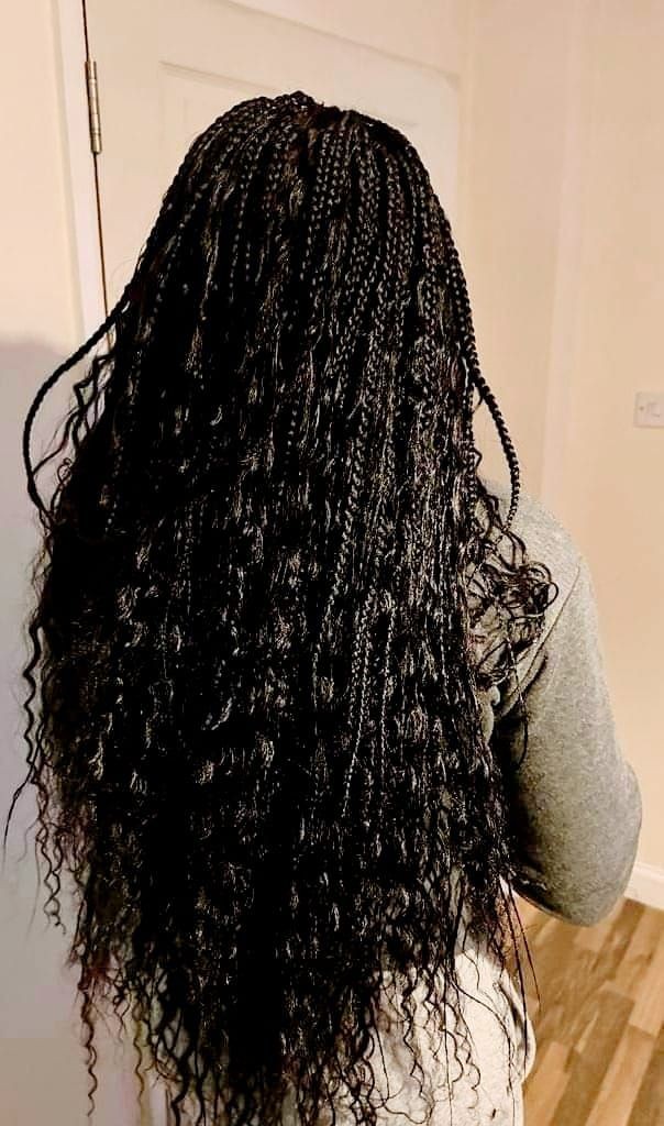 Person with long, intricately braided black hair standing indoors facing away from the camera.